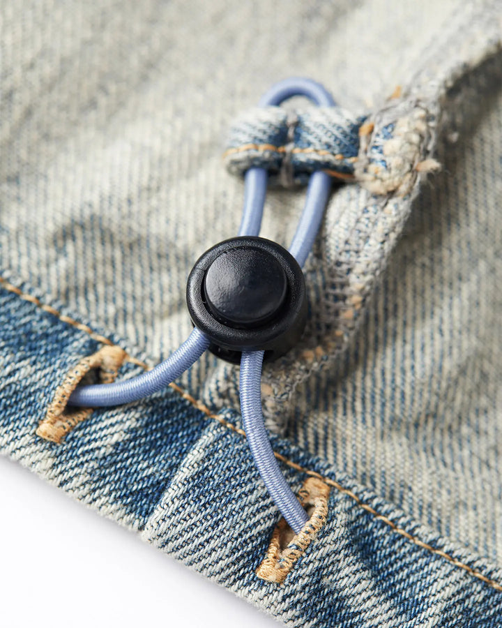 Gros plan sur un jean en denim bleu délavé avec cordon élastique réglable et bouton noir, matière 100 % coton, style décontracté et confortable pour femme.