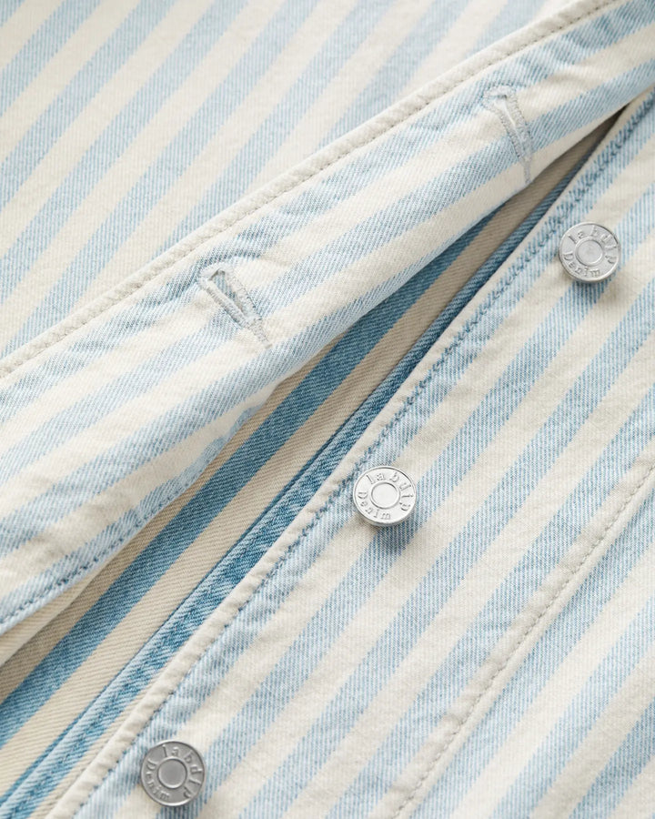 Détail rapproché d’un jean en denim rayé bleu indigo et beige, matière en coton, finition boutons-pression métalliques, coupe ajustée pour femme.