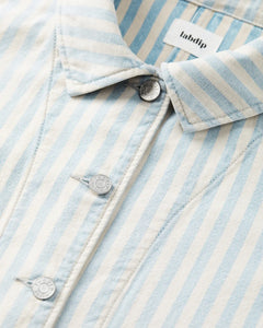Détail d'une veste en denim léger rayé bleu ciel et écru, avec boutons métalliques gravés Labdip, tissu en coton structuré et coupe ajustée.