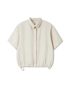 Chemisier femme écru en tissu fluide et léger, coupe ample avec manches courtes larges et bas resserré par un cordon ajustable pour un style décontracté.