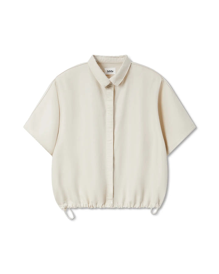 Chemisier femme écru en tissu fluide et léger, coupe ample avec manches courtes larges et bas resserré par un cordon ajustable pour un style décontracté.