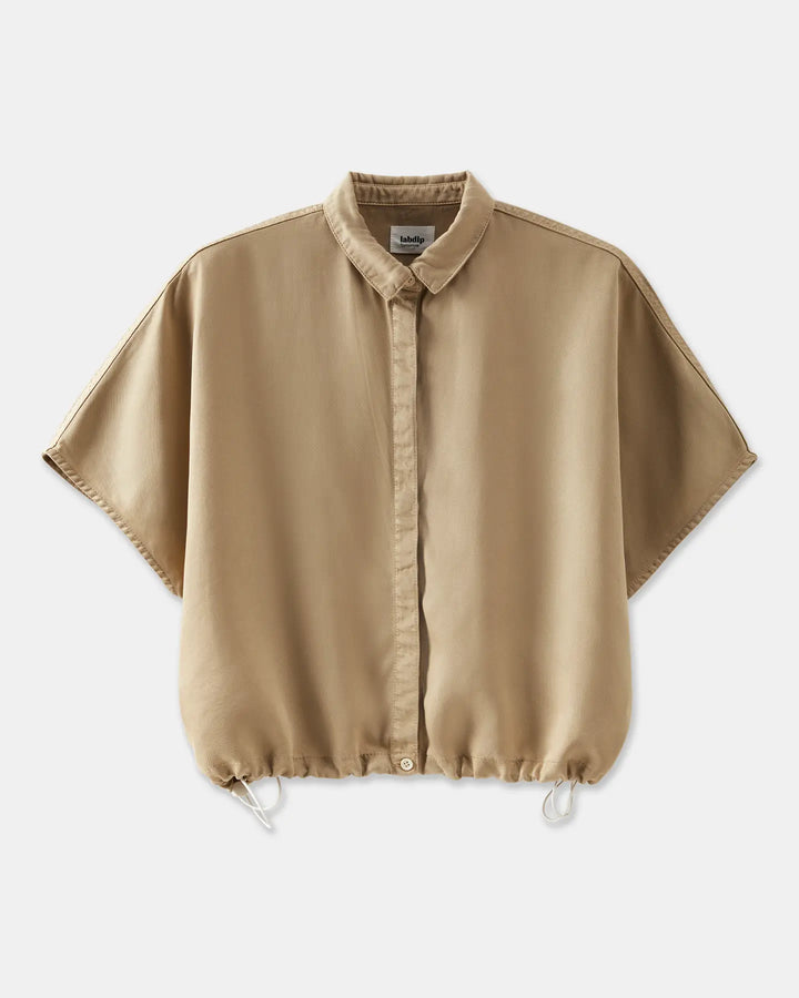 Chemise femme beige en tissu fluide avec coupe ample, col classique et bas resserré par un cordon ajustable.
DEVA chemise
