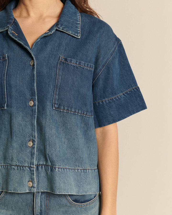 Chemise en denim bleu délavé en coton, coupe droite avec manches courtes larges, idéal pour un style estival décontracté et confortable.