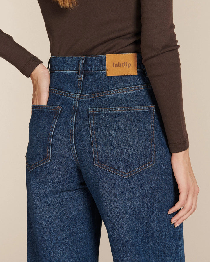 Jean ballon en denim bleu moyen 100% coton avec taille haute et poches arrière carrées, conçu pour s'adapter à toutes les morphologies féminines.
Porté par le mannequin de dos