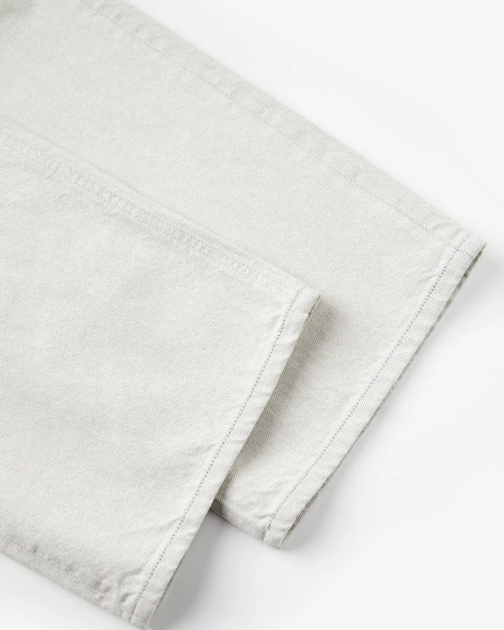 Détail en gros plan d’un jean en denim 100 % coton de couleur granit claire avec une coupe droite et une finition brute au bas des jambes.
