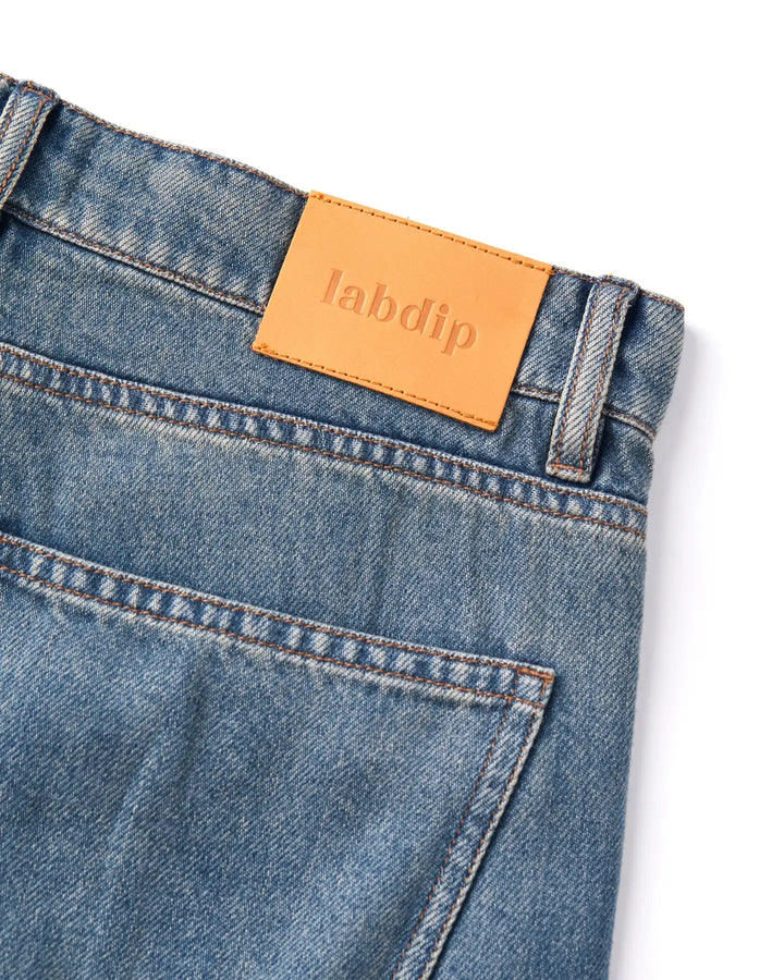 Jean en denim bleu légèrement délavé, coupe droite classique avec poche arrière, ceinture renforcée et étiquette en cuir avec logo Labdip.