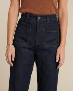 Jean femme en denim brut bleu foncé, coupe droite légèrement ample avec poches plaquées frontales et couture contrastée, en coton robuste et confortable.