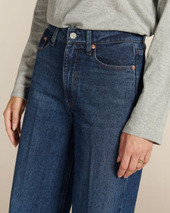 Jean long droit en denim bleu stone, 100% coton, aux finitions classiques avec coutures contrastantes, conçu pour s’adapter à toutes les morphologies féminines.
Jean droit large SULLY porté par le mannequin, détail de la taille et des poches.